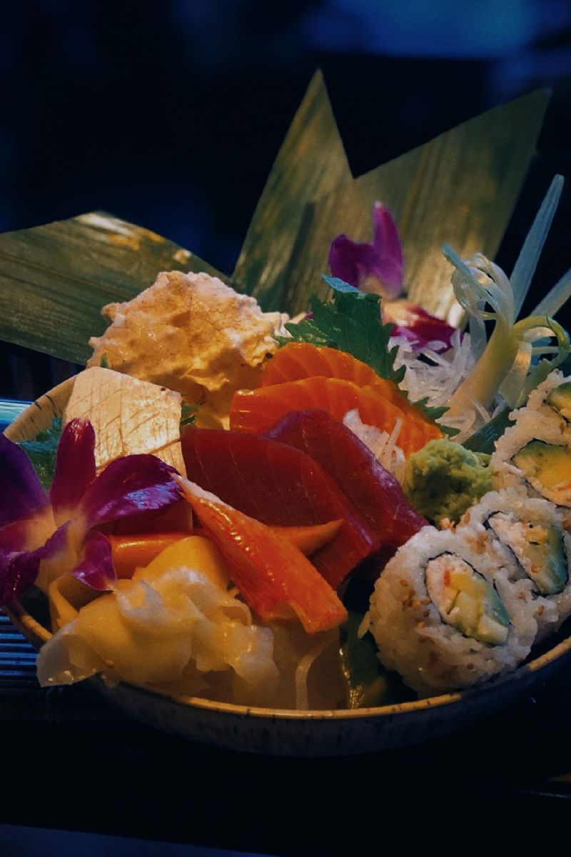 Bowl of salmon and tuna sashimi with rolls and orchids